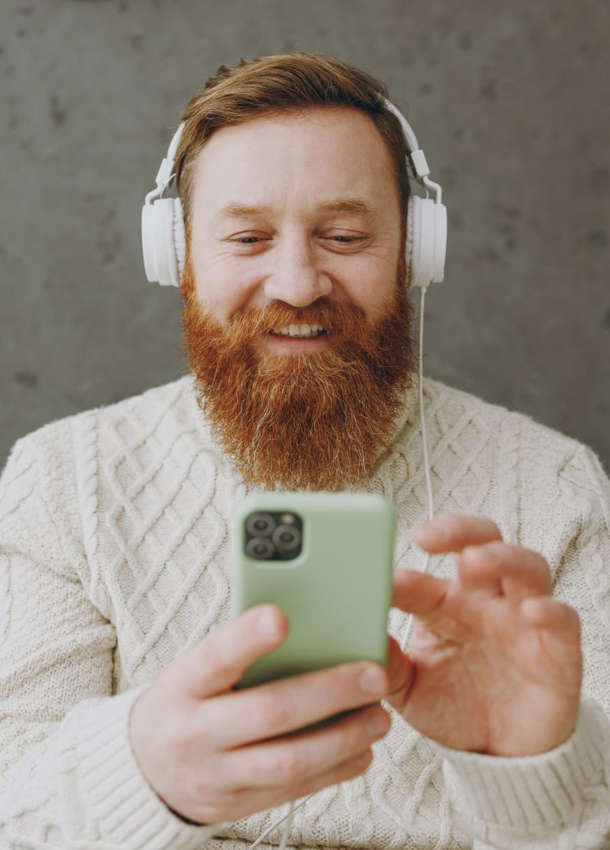 Happy bearded man browsing on phone while wearing headphones