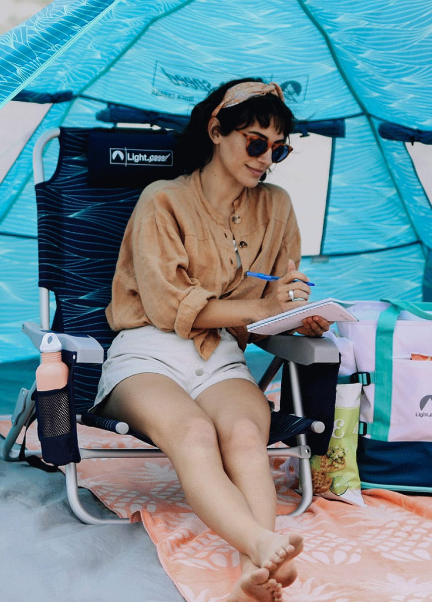 Woman sitting in Lightspeed beach chair writing in notebook